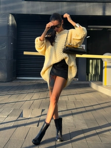 Outdoor street view of a pale yellow cable-knit sweater paired with a black skirt