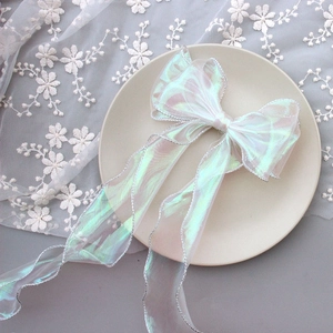 Detail of a large iridescent organza bow hair clip with silver glitter edges on lace fabric