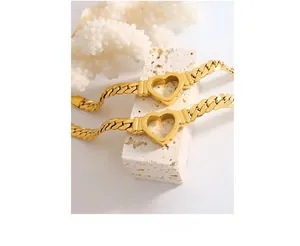 Detailed view of two gold chunky chain bracelets with a hollow heart charm on marble
