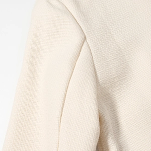 Dettaglio del tessuto beige con cuciture pulite su una giacca corta stile francese