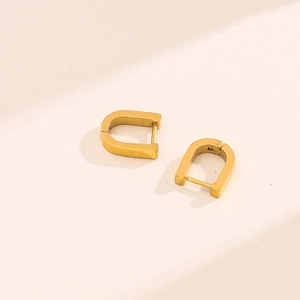 Boucles d'oreilles créoles minimalistes en forme de U dorées sur fond beige chaud