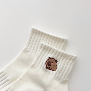 Dettaglio ravvicinato della calza in cotone bianco con ricamo a forma di capibara