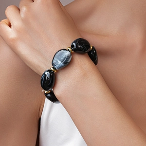 Macro detail of acrylic irregular oval beaded bracelet with gold metal accents on wrist