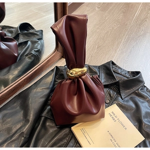 Detailed macro view of burgundy leather handbag with textured folds and gold metal handle knot