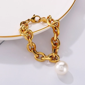Close-up of a gold chunky chain bracelet with a single round white pearl on a porcelain plate