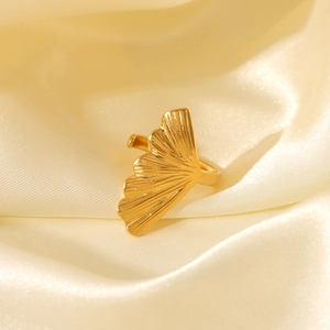 Detail view of a golden ginkgo leaf stainless steel ring on elegant cream silk fabric