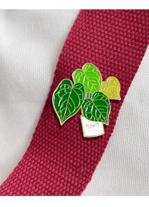 Macro view of a green potted plant enamel brooch with Plants text on a wine red ribbon