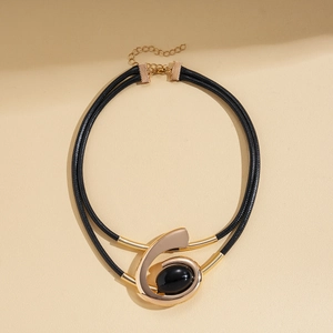 Detail of double-layer black choker necklace with gold spiral pendant and black resin stone