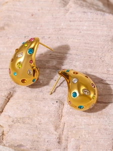 Detail shot of golden teardrop earrings with multi-color cubic zirconia on stone background