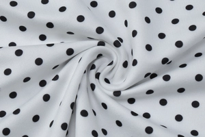 Close-up of white knitted fabric with black polka dots showing soft texture and weave