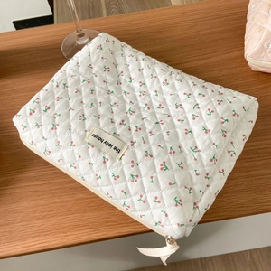 Detail of white quilted cherry cosmetic bag with white ribbon zipper and branded label
