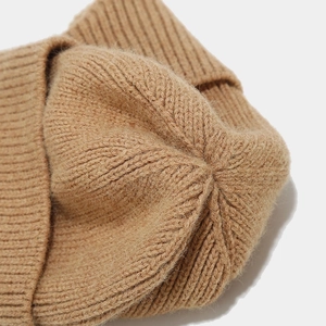 Macro detail of the coarse knit texture and top stitching on a warm camel beanie hat