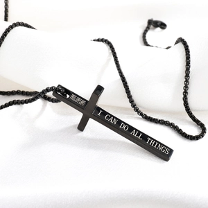 Macro shot of matte black cross necklace with bible verse engraving on white silk