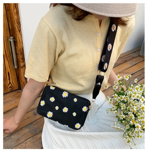 Floral crossbody bag with daisy prints and wide shoulder strap shown on a model