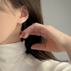 Close-up of small silver textured hoop earrings worn on ear showing irregular design