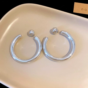 Close-up of minimalist silver twisted C-shaped hoop earrings on a beige tray