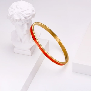 Detail of gold-plated stainless steel bangle with red enamel inlay on white pedestal