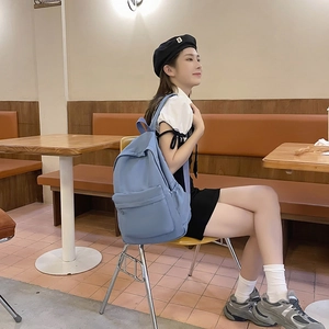 Minimalist blue nylon backpack with large capacity worn by a woman in a cafe setting