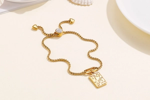 Detail of adjustable gold bracelet with rectangular charm and embossed fashion symbols