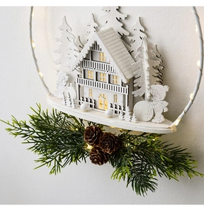 Detail of white wooden Christmas ornament with LED lights, house, and pine cones
