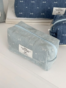 Detail of light blue denim makeup bag with white bow embroidery and zipper closure