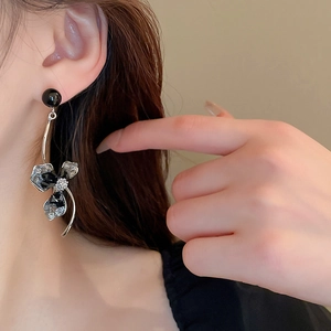 Close-up of asymmetric black crystal flower earrings with long drop pearl design