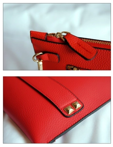 Detail van rode clutch met lychee leerstructuur, gouden rits en metalen klinknagels