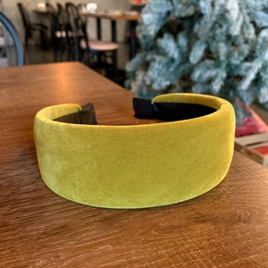 Detailed view of thick velvet sponge headband in mustard green on a wooden surface