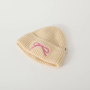 Berretto in maglia beige per neonati con fiocco rosa ricamato su sfondo bianco