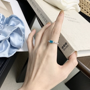 Detail of a silver ring featuring a blue rectangular stone on a model's hand with silk props