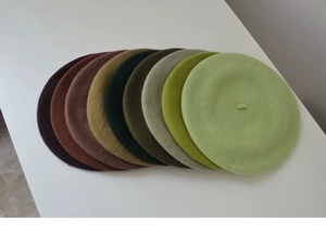 Detailed close-up showing a stack of thick wool berets in various green and brown tones