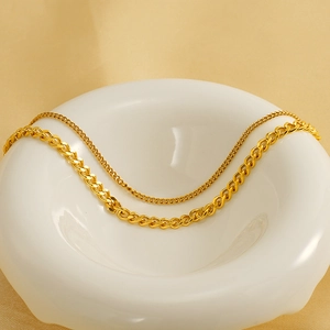 Detail of layered gold stainless steel necklace with fine link and flat Cuban chains