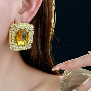 Dettaglio di grandi orecchini quadrati dorati con cristallo ovale giallo e pavé di diamanti