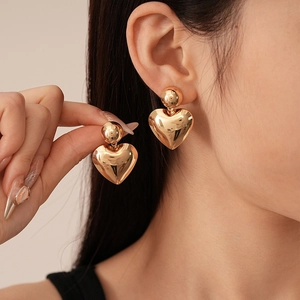Detail of elegant gold geometric heart drop earrings with polished metallic sphere stud