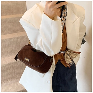 Detail of dark brown suede shoulder bag featuring a metallic fashion logo and wide strap
