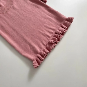 Pink knit sweater with ruffle hem and ribbed crew neck displayed on flat background