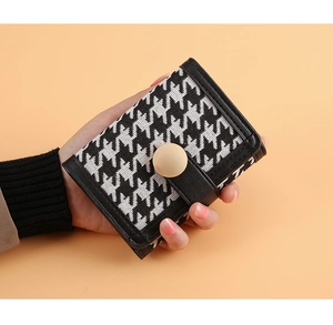 Detail view of houndstress fabric texture and round beige button on a chic black wallet