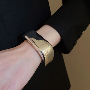 Close-up of chunky gold wave cuff bracelet on model's wrist with polished metallic finish