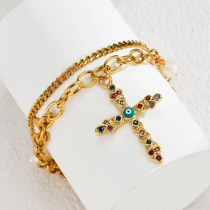 Close-up of double-layer gold cross necklace with pearl and evil eye gemstone details