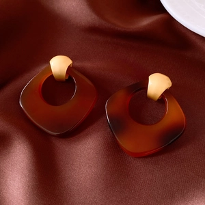 Gros plan de boucles d'oreilles évidées en acétate sur un fond en satin luxueux