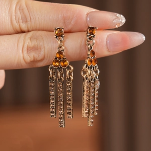 Macro detail of vintage bronze-tone dangle earrings with amber rhinestones and tassels