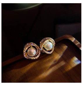 Macro shot of gold spiral stud earrings featuring white pearl and crystal halo detail