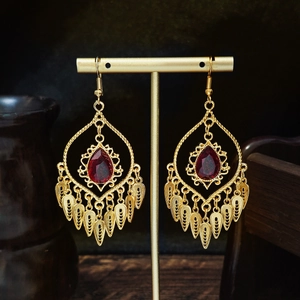 Bohemian geometric gold tassel earrings with red teardrop gemstone on dark wood