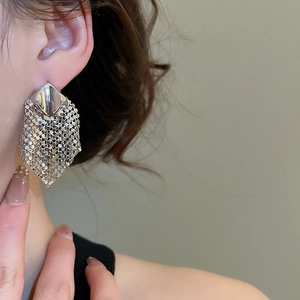 Macro shot of silver diamond-shaped sequin tassel earrings worn by a female model