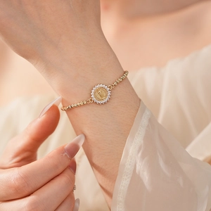 Détail d'un bracelet doré avec un médaillon religieux serti de zircons brillants et élégants