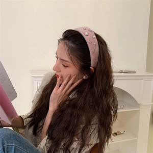 Pink plush headband with rhinestones and pearls worn by a woman in a cozy setting