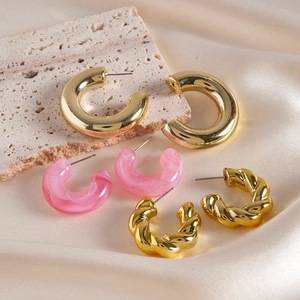 Three pairs of stylish gold and pink resin hoop earrings on beige silk fabric background
