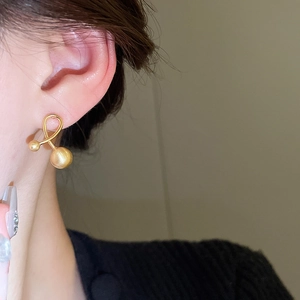 Close-up of gold-plated cross ball earrings showing matte texture and modern fit