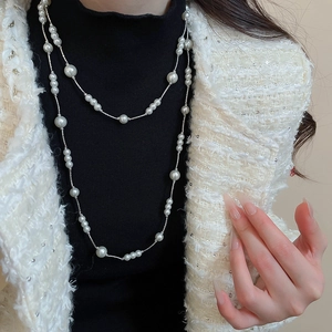 Close-up of layered long pearl necklace worn over black turtleneck and tweed jacket