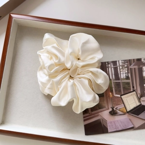Detailed view of the creamy satin scrunchie with soft silk texture and elegant pleats